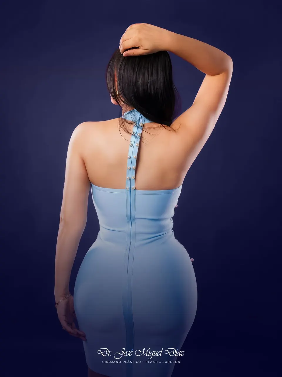 A patient of Dr. José Miguel Díaz from behind in a fitted blue dress, studio session.